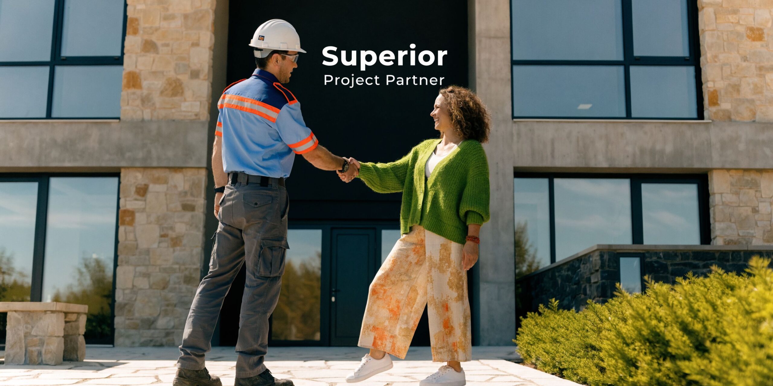 A construction worker and a female homeowner shake hands in front of a modern residential building project.